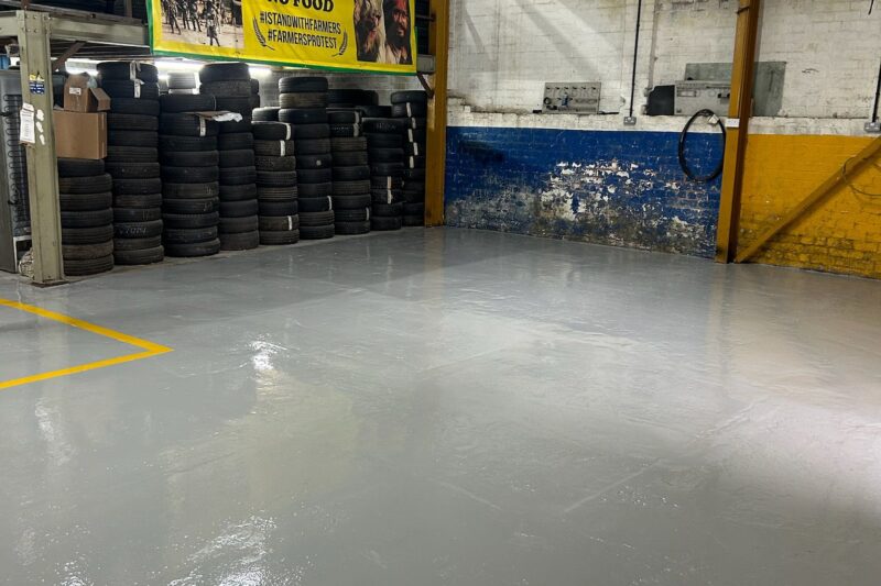 Finished commercial garage floor with a smooth, seamless epoxy resin coating and yellow safety line, providing a durable, professional surface ready for heavy-duty use.