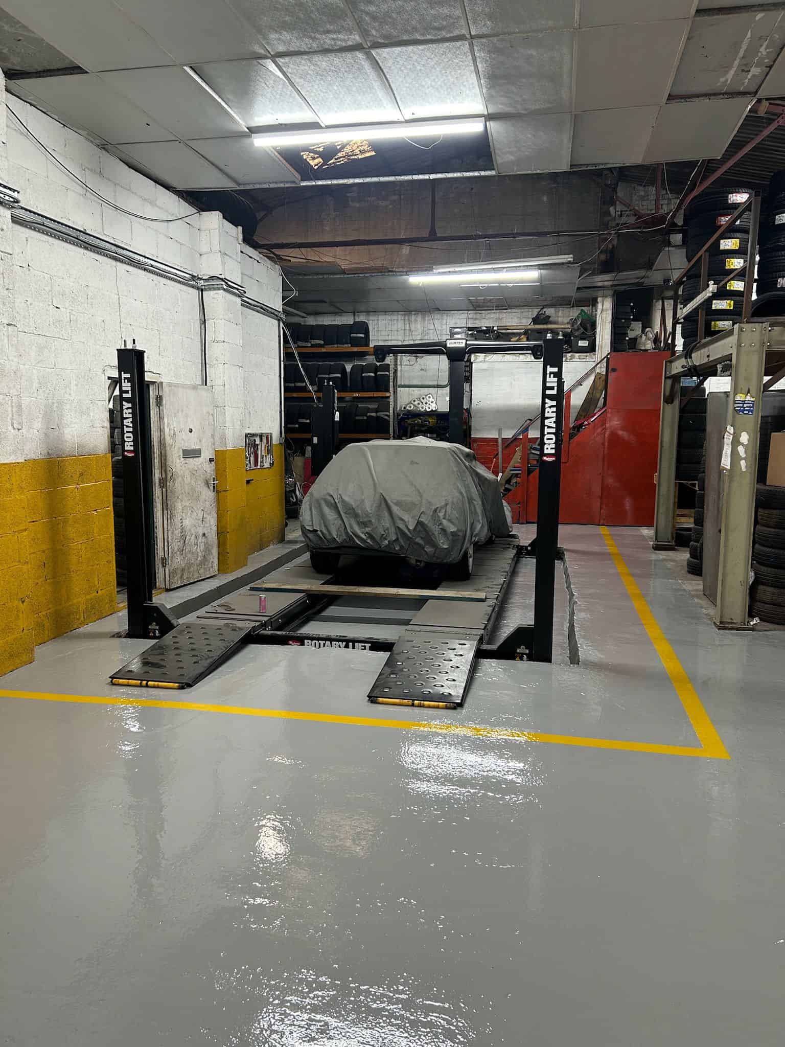 Finished commercial garage floor with a smooth, seamless epoxy resin coating and yellow safety line, providing a durable, professional surface ready for heavy-duty use.