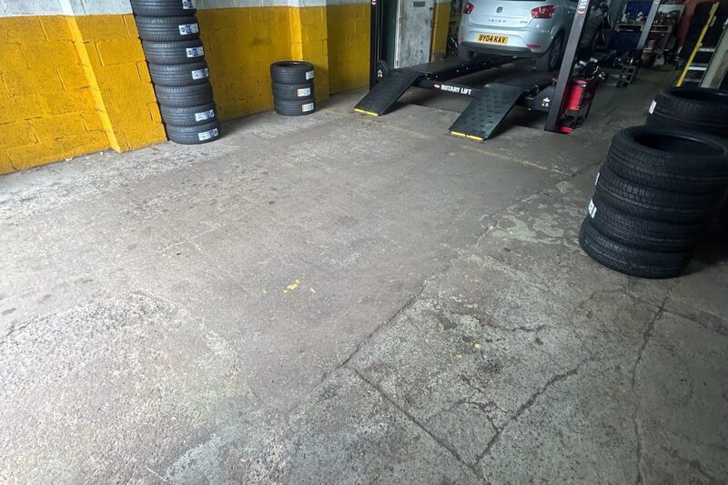 Cracked and damaged commercial garage floor in need of repair before epoxy resin coating application showing visible wear and surface imperfections